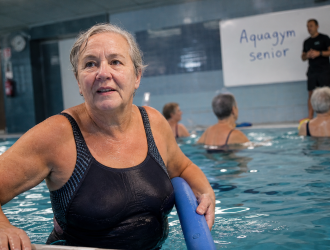 Aquagym senior en piscine : femme senior tient l’équilibre près du bord
